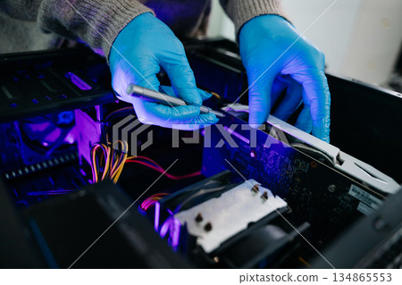 Computer technician in gloves safely repairing desktop hardware. Close-up view of hands fixing GPU and motherboard inside open PC case. Perfect for tech and repair concepts. 134865553
