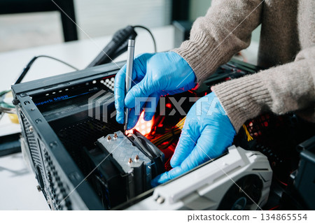 Computer technician in gloves safely repairing desktop hardware. Close-up view of hands fixing GPU and motherboard inside open PC case. Perfect for tech and repair concepts. Computer technician in gloves safely repairing desktop hardware. Close-up view of hands fixing GPU and motherboard inside open PC case. Perfect for tech and repair concepts. 134865554