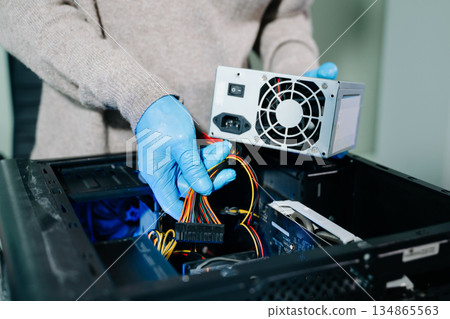 Computer technician in gloves safely repairing desktop hardware. Close-up view of hands fixing GPU and motherboard inside open PC case. Perfect for tech and repair concepts. 134865563