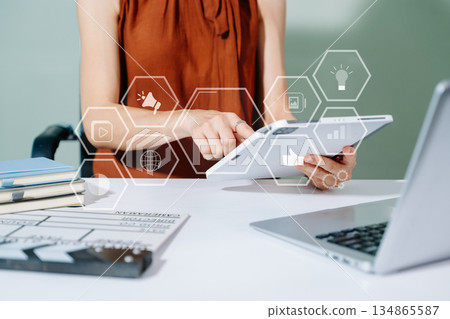 Creative female filmmaker working with tablet, clapperboard, and laptop in modern studio office. Film production, planning, and content creation scene. 134865587