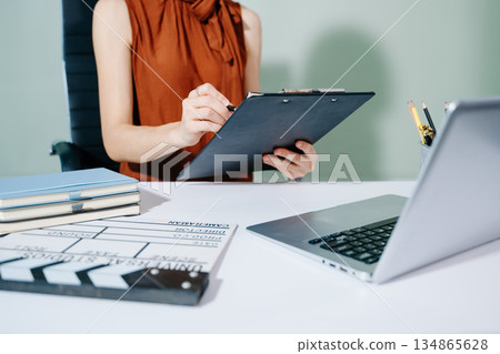Creative female filmmaker working with tablet, clapperboard, and laptop in modern studio office. Film production, planning, and content creation scene. Creative female filmmaker working with tablet, clapperboard, and laptop in modern studio office. Film production, planning, and content creation scene. 134865628