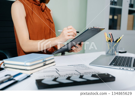 Creative female filmmaker working with tablet, clapperboard, and laptop in modern studio office. Film production, planning, and content creation scene. Creative female filmmaker working with tablet, clapperboard, and laptop in modern studio office. Film production, planning, and content creation scene. 134865629