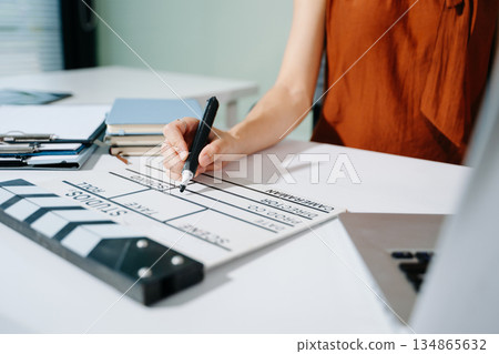 Creative female filmmaker working with tablet, clapperboard, and laptop in modern studio office. Film production, planning, and content creation scene. 134865632