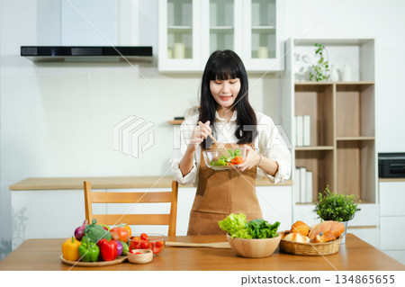 Asian woman prepares healthy salad with fresh vegetables in a modern kitchen. Clean, vibrant, and perfect for nutrition, lifestyle, or home cooking concepts. Asian woman prepares healthy salad with fresh vegetables in a modern kitchen. Clean, vibrant, and perfect for nutrition, lifestyle, or home cooking concepts. 134865655