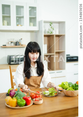Asian woman prepares healthy salad with fresh vegetables in a modern kitchen. Clean, vibrant, and perfect for nutrition, lifestyle, or home cooking concepts. Asian woman prepares healthy salad with fresh vegetables in a modern kitchen. Clean, vibrant, and perfect for nutrition, lifestyle, or home cooking concepts. 134865656
