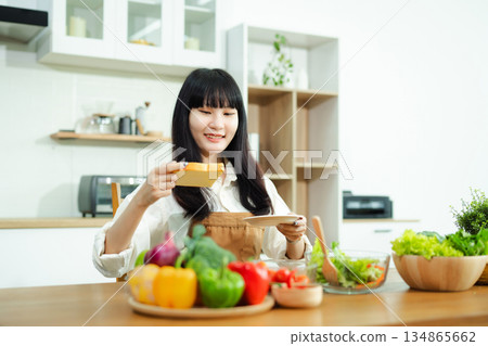 Asian woman prepares healthy salad with fresh vegetables in a modern kitchen. Clean, vibrant, and perfect for nutrition, lifestyle, or home cooking concepts. Asian woman prepares healthy salad with fresh vegetables in a modern kitchen. Clean, vibrant, and perfect for nutrition, lifestyle, or home cooking concepts. 134865662