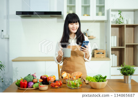 man holds coffee and checks smartphone in modern kitchen with fresh vegetables and bread. A cheerful scene of tech, breakfast, and wellness lifestyle at home. man holds coffee and checks smartphone in modern kitchen with fresh vegetables and bread. A cheerful scene of tech, breakfast, and wellness lifestyle at home. 134865687
