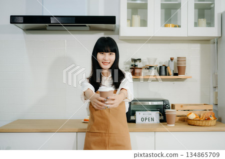 Young Asian woman coffee shop owner holding notepad and digital tablet ready to receive orders in cafe restaurant. Young Asian woman coffee shop owner holding notepad and digital tablet ready to receive orders in cafe restaurant. 134865709
