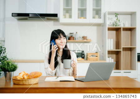 Woman using laptop while sitting at home. Young woman sitting in kitchen Woman using laptop while sitting at home. Young woman sitting in kitchen 134865743
