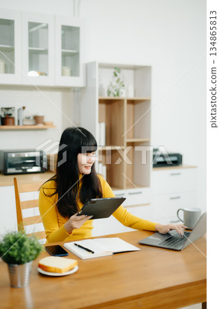 Portrait of young asian woman using laptop with sitting working on laptops and tablets in a cozy workspace. i Portrait of young asian woman using laptop with sitting working on laptops and tablets in a cozy workspace. i 134865813