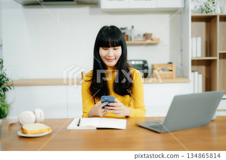 Portrait of young asian woman using laptop with sitting working on laptops and tablets in a cozy workspace. i Portrait of young asian woman using laptop with sitting working on laptops and tablets in a cozy workspace. i 134865814