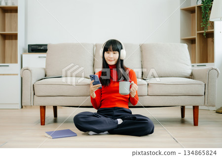 Young asian woman using smartphone and tablet while seated on couch 134865824
