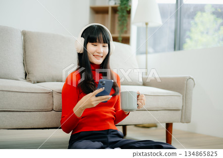 Young asian woman using smartphone and tablet while seated on couch 134865825