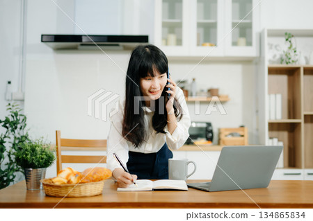 Woman using laptop while sitting at home. Young woman sitting in kitchen 134865834