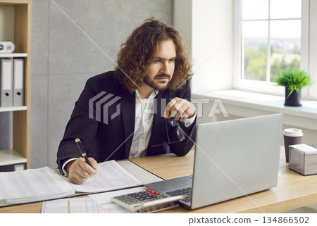 Bearded business man working at the desk on workplace at office looking at laptop monitor screen. 134866502