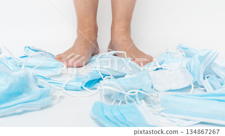 Feet standing on a chaotic pile of discarded medical face masks, symbolizing the environmental impact of single-use items and the urgent need for sustainable practices in healthcare and personal 134867267