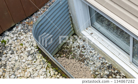 Exterior view of a drainage system with gravel and metal edging, showcasing water management features and landscaping elements for home improvement 134867282