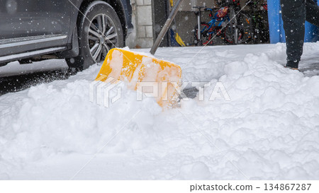 Snow storm scene with a bright yellow shovel clearing thick snow from a driveway, showcasing winter weather challenges and outdoor activity Snow storm scene with a bright yellow shovel clearing thick snow from a driveway, showcasing winter weather challenges and outdoor activity 134867287