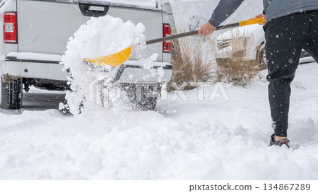 Snow cleaning service worker shoveling snow from driveway near parked truck, showcasing winter maintenance and outdoor labor efforts 134867289