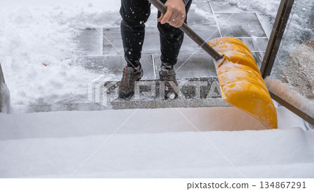 Individual shoveling snow from steps with a bright yellow shovel, surrounded by a winter landscape, showcasing the effort of snow removal Individual shoveling snow from steps with a bright yellow shovel, surrounded by a winter landscape, showcasing the effort of snow removal 134867291