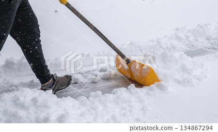 Snow cleaning service worker using a yellow shovel to clear snow from a walkway during a winter storm, showcasing effective snow removal techniques 134867294