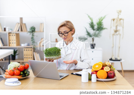 A nutritionist is holding microgreens while consulting online about healthy eating and diet. A nutritionist is holding microgreens while consulting online about healthy eating and diet. 134871284