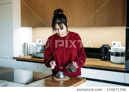 Woman scoops coffee grounds into moka pot base on wooden counter. Decaf espresso brewing, caffeine free lifestyle, healthy morning habits. 134871306