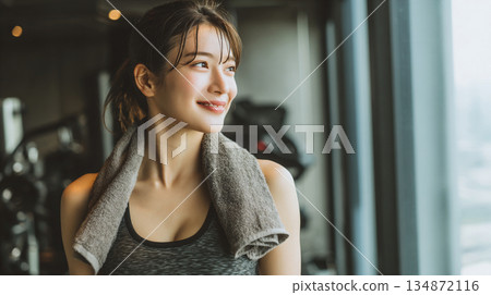 Smiling woman with towel draped over her shoulders at the gym (AI-generated) 134872116