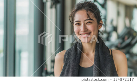 Smiling woman with towel draped over her shoulders at the gym (AI-generated) 134872117