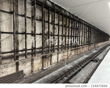 Metro station reconstruction in progress. Concrete wall with metal frame near railway track at station. Metro station renovation in progress. Wall cladding 134873694
