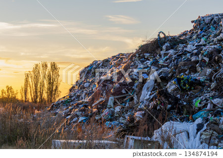 Large piles of garbage rise in the background as the sun sets, casting an orange glow over a landfill in a rural area 134874194