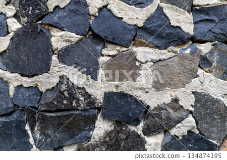 Close view of a stone wall with different shapes and colors of rock pieces fitted together in a unique pattern Close view of a stone wall with different shapes and colors of rock pieces fitted together in a unique pattern 134874195