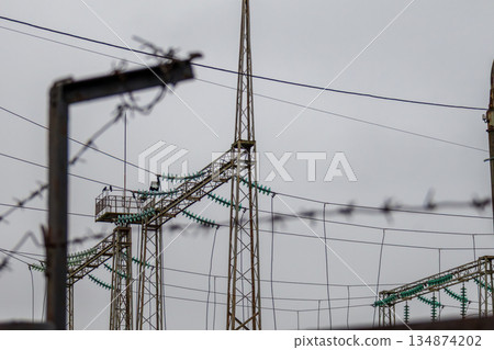 Electricity towers stand tall behind a barbed wire fence on an overcast day in an industrial zone 134874202