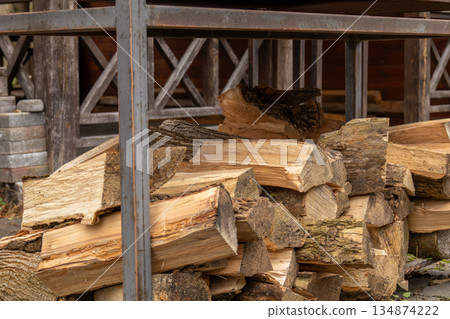Logs of wood are neatly arranged under a metal frame outside a wooden building during daylight hours Logs of wood are neatly arranged under a metal frame outside a wooden building during daylight hours 134874222
