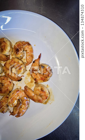 Hibachi grilled shrimp curled on white plate, brushed with a golden garlic butter glaze and teriyaki sauce. This savory seafood appetizer is perfect for gatherings, offering a warm aroma 134874310