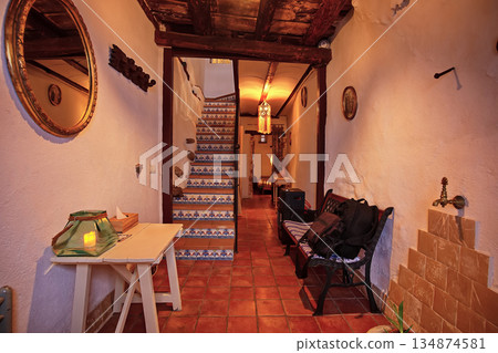Cozy rustic hallway with tiled stairs, warm lighting, and seating area in a Mediterranean style home Cozy rustic hallway with tiled stairs, warm lighting, and seating area in a Mediterranean style home 134874581
