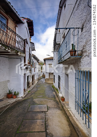 Narrow whitewashed village street with blue balconies and potted plants under a sunny sky Narrow whitewashed village street with blue balconies and potted plants under a sunny sky 134874582
