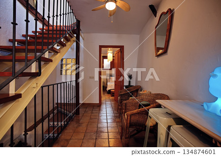 Cozy rustic hallway interior with wooden stairs, wicker chairs, and a blue glow lamp in a warm home setting 134874601