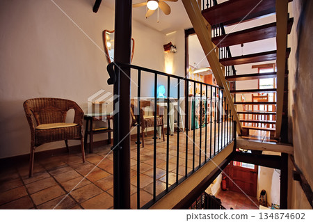 Cozy rustic interior with wicker chairs and a wooden staircase in a charming indoor cafee setting Cozy rustic interior with wicker chairs and a wooden staircase in a charming indoor cafee setting 134874602