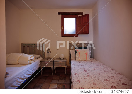 Cozy twin bedroom with rustic window, soft bedding, and nightstands in a small, charming room 134874607