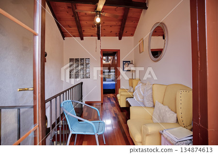 Cozy hallway living area with yellow armchairs, blue chair, and wooden beams leading to a bedroom 134874613