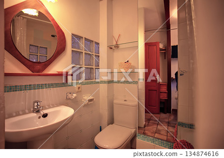 Cozy bathroom scene with sink, toilet and red door in warm, intimate setting 134874616