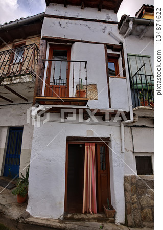 Rustic white building facade with wooden door, balcony, and potted plants on a narrow street 134874622