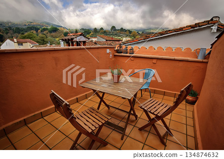 Cozy rooftop terrace with wooden table and chairs overlooking a scenic hillside village 134874632