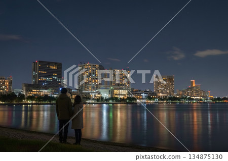 一對年輕情侶背影依偎在台場，欣賞夜景，享受著浪漫的約會時光。 134875130