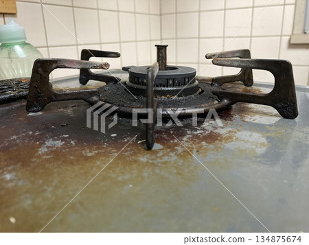 一台老式瓦斯爐，上面積滿了多年的油污和燒焦的食物殘渣。 134875674