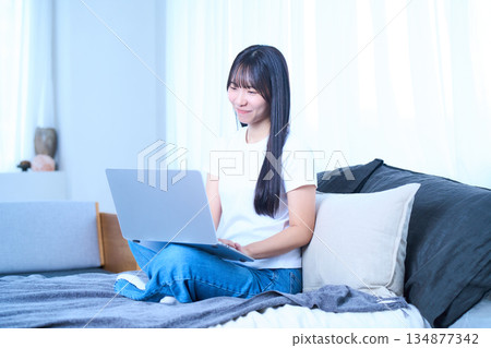 一位年輕女子正躺在床上放鬆地使用筆記型電腦。 一位年輕女子正躺在床上放鬆地使用筆記型電腦。 134877342