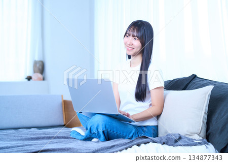 一位年輕女子正躺在床上放鬆地使用筆記型電腦。 一位年輕女子正躺在床上放鬆地使用筆記型電腦。 134877343