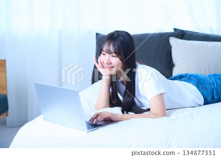 一位年輕女子正躺在床上放鬆地使用筆記型電腦。 134877351