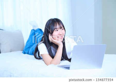 一位年輕女子正躺在床上放鬆地使用筆記型電腦。 一位年輕女子正躺在床上放鬆地使用筆記型電腦。 134877354
